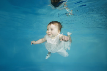 Little girl in a white dress swims underwater in a swimming pool