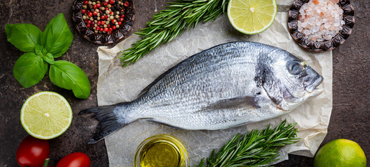 Fresh ready to cook raw bream fish dorado with ingredients and seasonings like rosemary, salt, pepper, lime and olive oil, top view