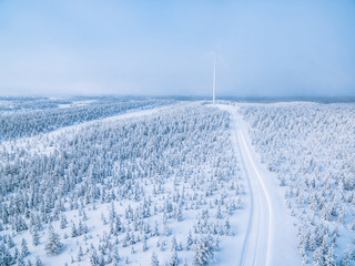 Aerial view of windmill in winter forest with snow road in Finland.