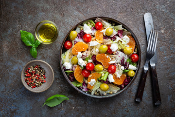 Fresh green mixed salad leaves frisee, radicchio and lamb's lettuce with tomato, olives and tangerine in a plate, top view.