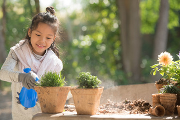 adorable 8 years old asian little girl is watering plant in pots in garden outside house, child education of nature. caring for a new life. earth day holiday concept. world environment day. ecology.