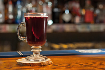 Red cocktail on bar counter. Drink with wine, fruit and cinnamon on the background of bottles with alcohol. Glass with booze on a wooden board.