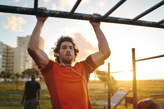 Portrait of a young crossfit sportsman exercising on bar, doing pull-ups for arms and back muscles at the outdoor gym park