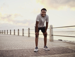 Portrait of a tired smiling young sportive man taking break after jogging on seaside promenade