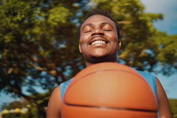 Portrait of a smiling satisfied young male player with eyes closed holding basketball at outdoors