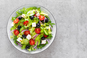 Salad with fresh raw vegetables, cucumber, tomato, olive, onion, lettuce and feta cheese, greek cuisine, healthy food, top view.