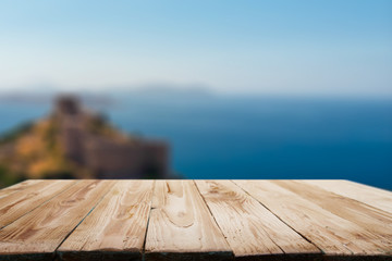 Wooden empty surface on blurred background of coastal sea, hill in afternoon.
