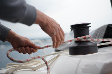 Hands of a man coiling up a rope, the halyard on a sailboat