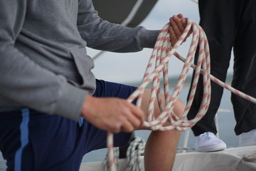 Hands of a man coiling up a rope, the halyard on a sailboat