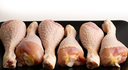 Raw chicken legs on a black plate. White background. Isolated. 