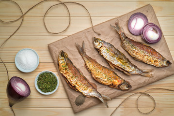 delicious fried small fish with spices on craft paper on a wooden table view from above