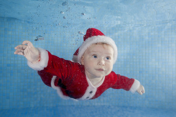 Little baby girl red New Year's dress swims underwater in a swimming pool