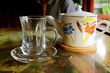 Transparent tea cup with a porcelain teapot on the table