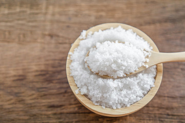 closeup salt in bowl with spoon on wooden table closeup