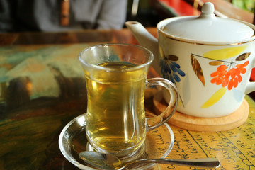 Hot herb tea in transparent cup with a porcelain teapot on the table