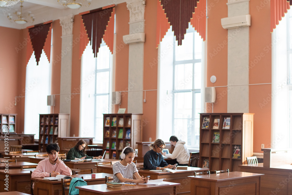 Poster Two rows of desks in college library and students working individually while preparing for seminar after classes