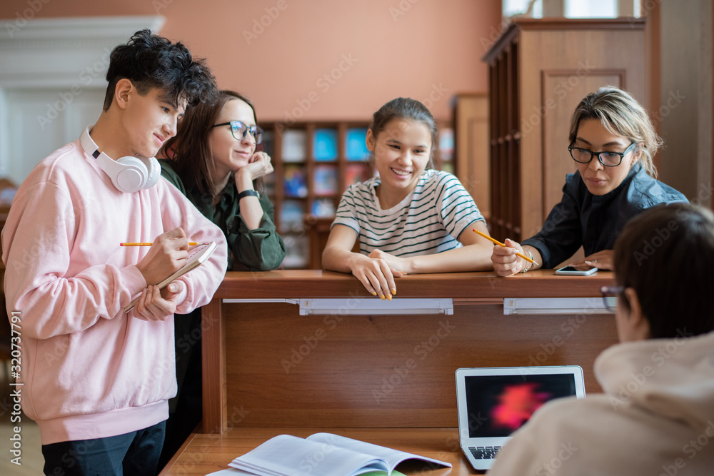 Poster Group of clever college student standing by programmer in front of laptop helping them to find information for seminar