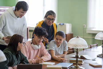 Obraz premium Two students pointing at notes of teenage guy in his notepad while choosing name for project in group in college library