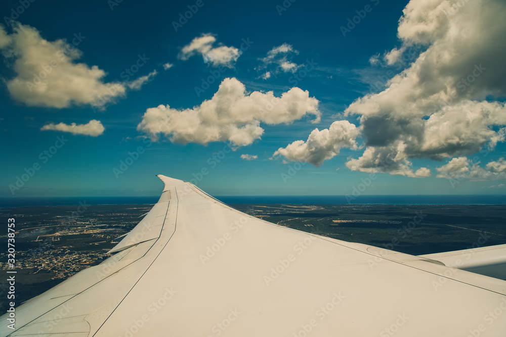 Wall mural Wing of an airplane flying above the sky with clouds and city land