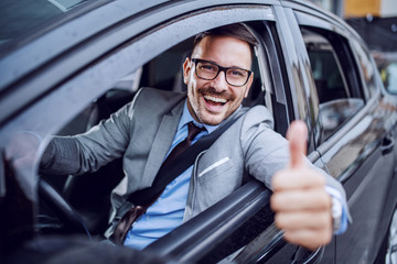 Handsome caucasian unshaven classy businessman in suit and with eyeglasses holding hand on steering...