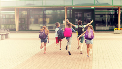 Obraz premium primary education, friendship, childhood and people concept - group of happy elementary school students with backpacks running outdoors