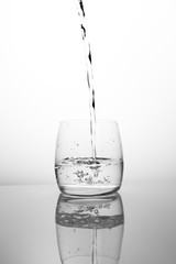 A stream of clean drinking water flows into a transparent glass. Black and white glass with water air bubbles. A bubbling stream of spring water, bubbling and scattering