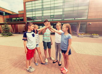 primary education, friendship, childhood and people concept - group of children or students making high five at school yard