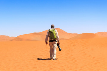 Man with backpack and big camera walking on the red sand dunes of Sossusvlei, Namib Naukluft Park, Namibia