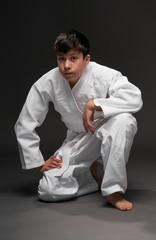 a teenager dressed in martial arts clothing sitting and thinking on a dark gray background, a sports concept