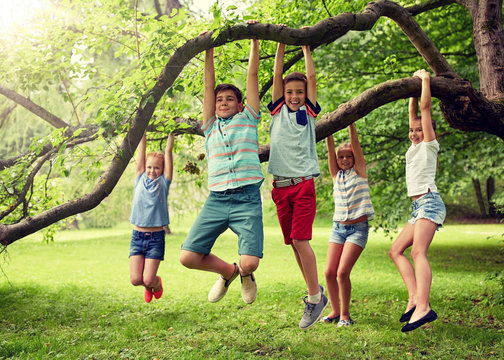 friendship, childhood, leisure and people concept - group of happy kids or friends hanging on tree and having fun in summer park