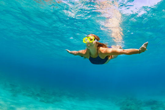 Active young woman in snorkeling mask dive, swim underwater