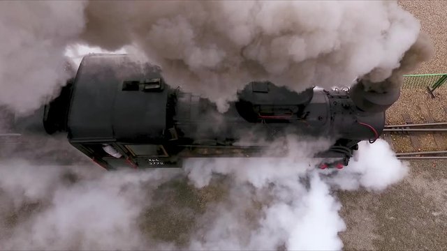 dron shot from above of old locomotive moving through railway, producing smoke