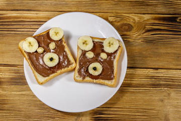 Two sweet sandwiches with delicious chocolate hazelnut spread and banana in shape of bear on wooden table. Top view
