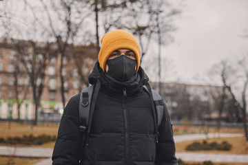 Fototapeta na wymiar Man in orange hat and black medical mask on the street. Coronavirus is a virus that is endemic in China. Protection from the illness for children. Health safety concept.