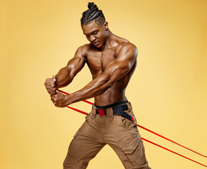 Athletic man performs exercises using resistance band. Photo of african american man on yellow...