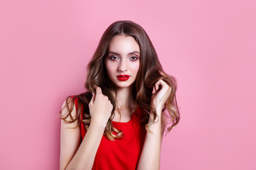 Beautiful woman with red lips, makeup and hairstyle in red dress on pink background