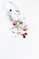 Multi-colored pills in a glass jar and scattered on a white background. Medical concept. Copy space.