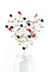 Multicolored pills spilled out of a glass jar in the shape of a heart on a white background. Medical health concept. Top view.
