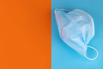 Medical mask on a blue background and copy space on an orange background. The concept of using personal protective equipment against coronavirus. View from above.