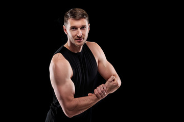 Fototapeta na wymiar Young strong athlete in black sportswear keeping one hand on wrist of the other while showing his strength in front of camera