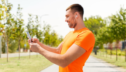 fitness, sport and people concept - smiling young man with smartphone and earphones listening to music at summer over city street on background