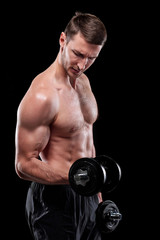 Fototapeta na wymiar Young muscular shirtless sportsman with dumbbells doing exercise for arms in isolation over black background