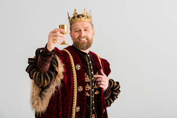 smiling king with crown holding cup isolated on grey - obrazy, fototapety, plakaty