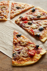 cut delicious italian pizza with olives on baking paper on wooden background