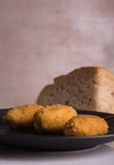 Three tasty homemade croquettes on a plate, accompanied by bread. Light background. Vertical format