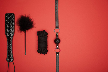 top view of black paddle, gag, rope, feather tickler isolated on red - obrazy, fototapety, plakaty