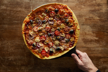 Cropped view of man holding pizza on wooden background