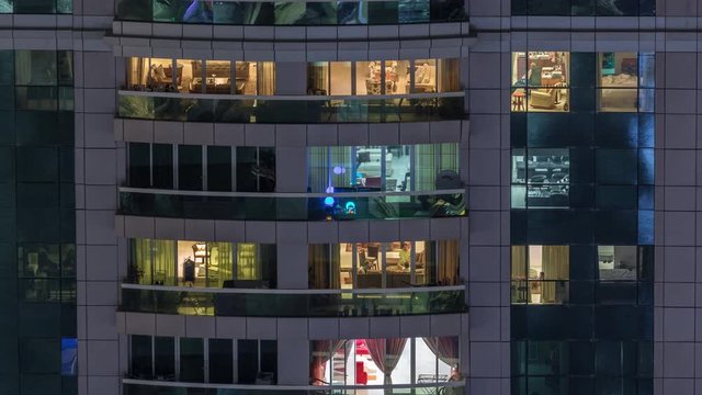 Night view of exterior apartment building timelapse. High rise skyscraper with blinking lights in windows with people moving inside. Zoom in