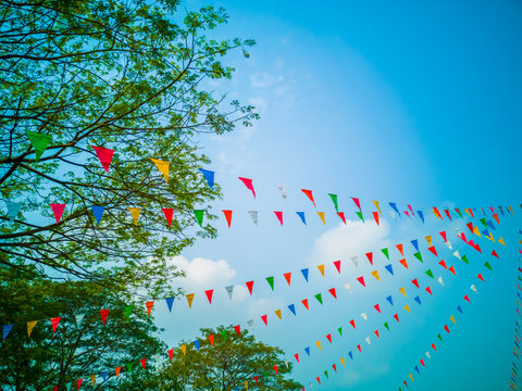 Colorful flags, colorful party decorations, small triangular flags to celebrate the party with the blue sky and clouds as the holiday concept background.