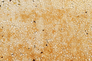 Background of an iron fence with peeled pieces of an old cracked shabby light paint layer and orange rust drips. Close up corrosion of metal on car body.